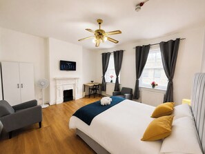 Una camera d'albergo con un letto, una scrivania, una sedia, un caminetto e una ventola a soffitto.