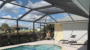 En swimmingpool med flydebolde, en overdækket terrasse og et hus i baggrunden.