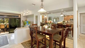 A dining area with a wooden table, chairs, and a chandelier. There is a kitchen visible through an open door. - Kaanapali Royal | 3 Ocean View Villas, Sleeps 17 | Car Incl. w/ 6+ Nights | ML-4688 by KBM (Lahaina)