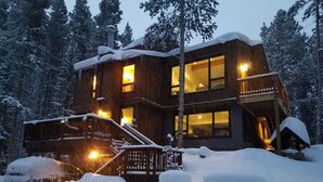 Eine mehrstöckige Holzhütte mit einem Balkon, umgeben von schneebedeckten Bäumen.