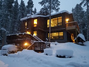 Una cabaña de madera de varios pisos con un balcón, rodeada de árboles cubiertos de nieve.
