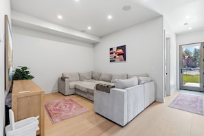 A modern living room with a grey sectional sofa, a wooden cabinet, a pink rug, and a painting on the wall. - Brand-New Frisco Townhome | Modern Mountain Retreat Near Ski Resorts (Frisco)