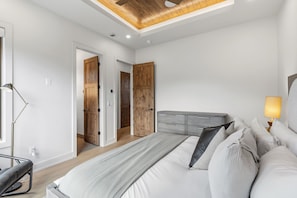 A modern bedroom with a large bed, wooden doors, and a ceiling with exposed beams. - Brand-New Frisco Townhome | Modern Mountain Retreat Near Ski Resorts (Frisco)