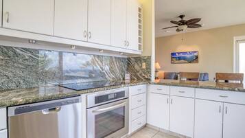 A kitchen with white cabinets, a granite countertop, a built-in oven, and a ceiling fan.