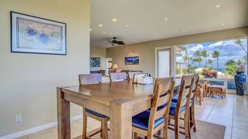 A dining area with a wooden table and chairs, a ceiling fan, and a view of the ocean.