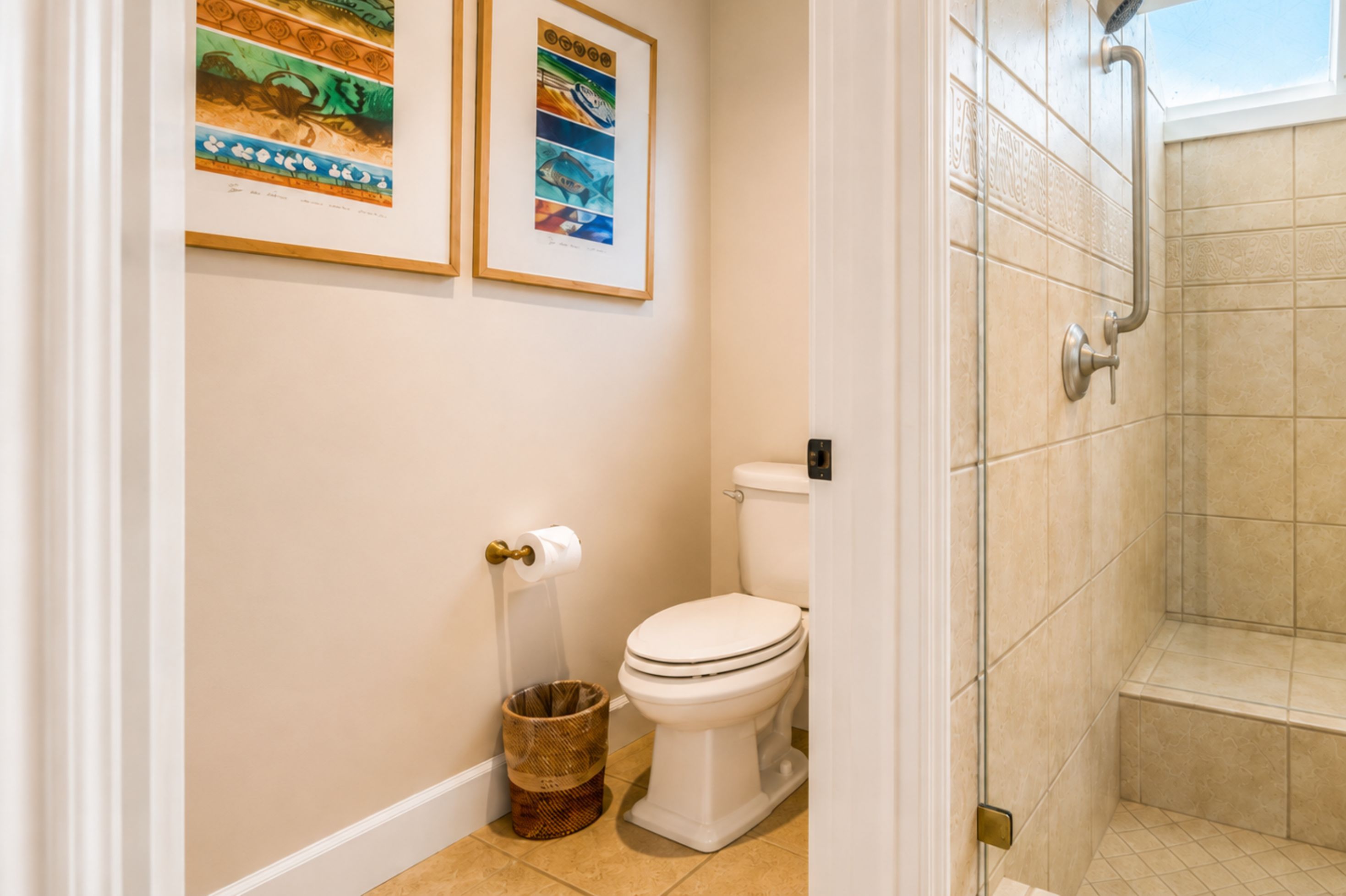 Een badkamer met toilet, een bidet, een douche en twee afbeeldingen in lijsten aan de muur.