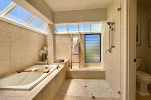 Een moderne badkamer met een badkuip, douche en toilet. Dakramen zorgen voor daglicht.