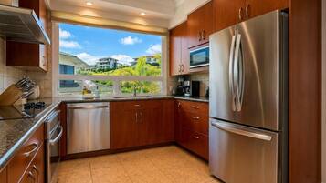 Your kitchen's window over the sink frames a lush hillside view, with stainless steel appliances, granite countertops, and rich wood cabinetry throughout. KBV-16B3