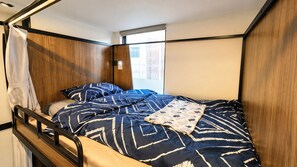 Een enkel bed met hoofdeinde, een raam met zonwering en een gordijn.