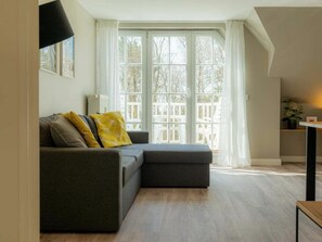 Ein modernes Wohnzimmer mit einem grauen Sofa, einem kleinen Tisch und einem Fenster mit weißen Vorhängen.