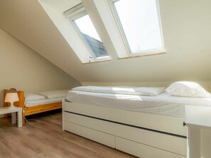 Ein Schlafzimmer mit schrägem Dach, einem Bett, einem Nachttisch und einer Lampe.