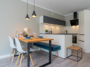 Eine moderne Küche mit Essbereich, ausgestattet mit einem Holztisch, weißen Stühlen und Pendelleuchten.