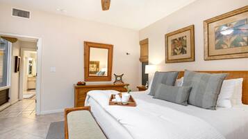 A hotel room with a large bed, a wooden headboard, a ceiling fan, a dresser, a mirror, and two framed artworks on the wall.