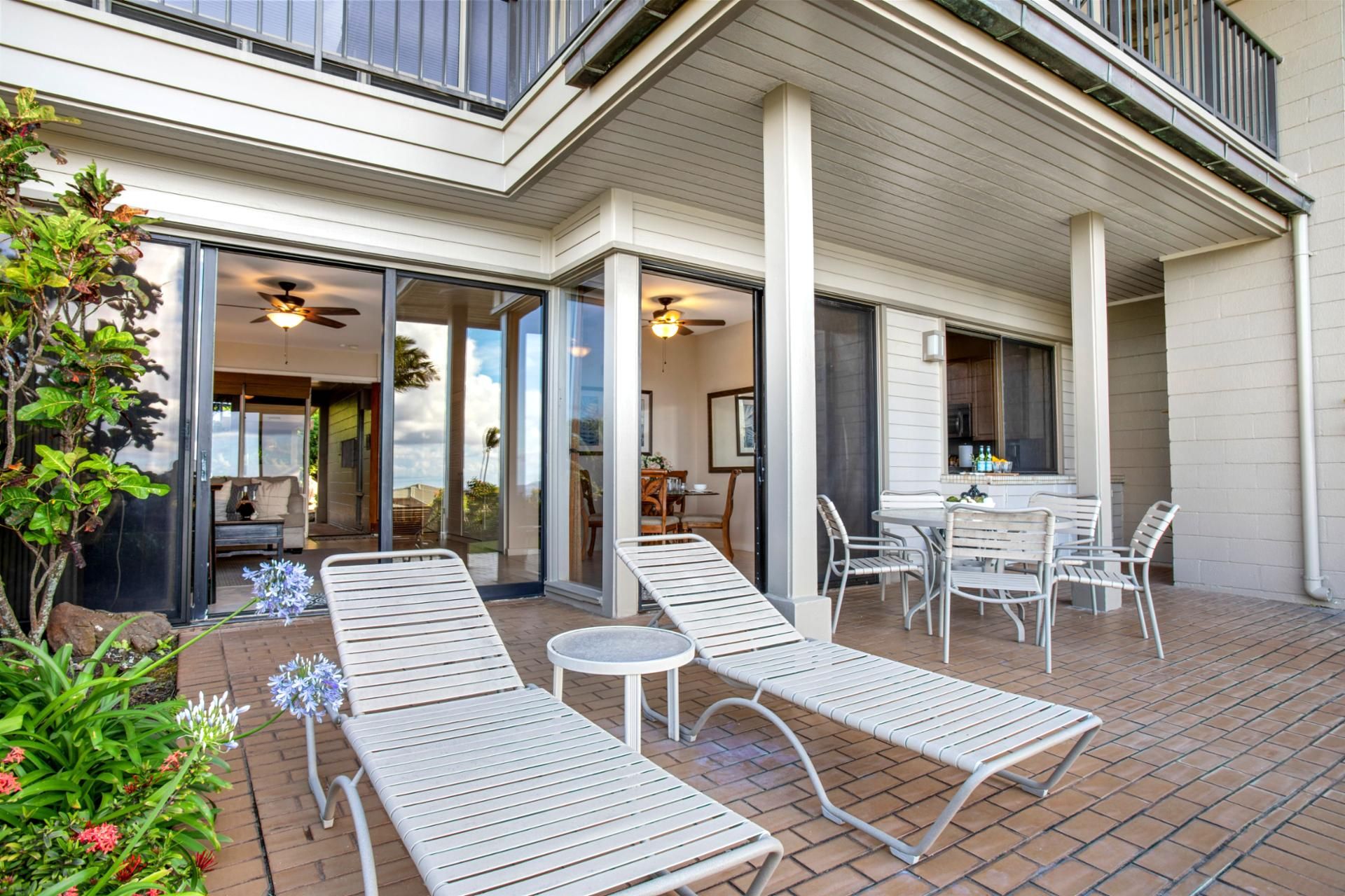 A modern outdoor patio with lounge chairs and a dining table, surrounded by a brick floor and potted plants.