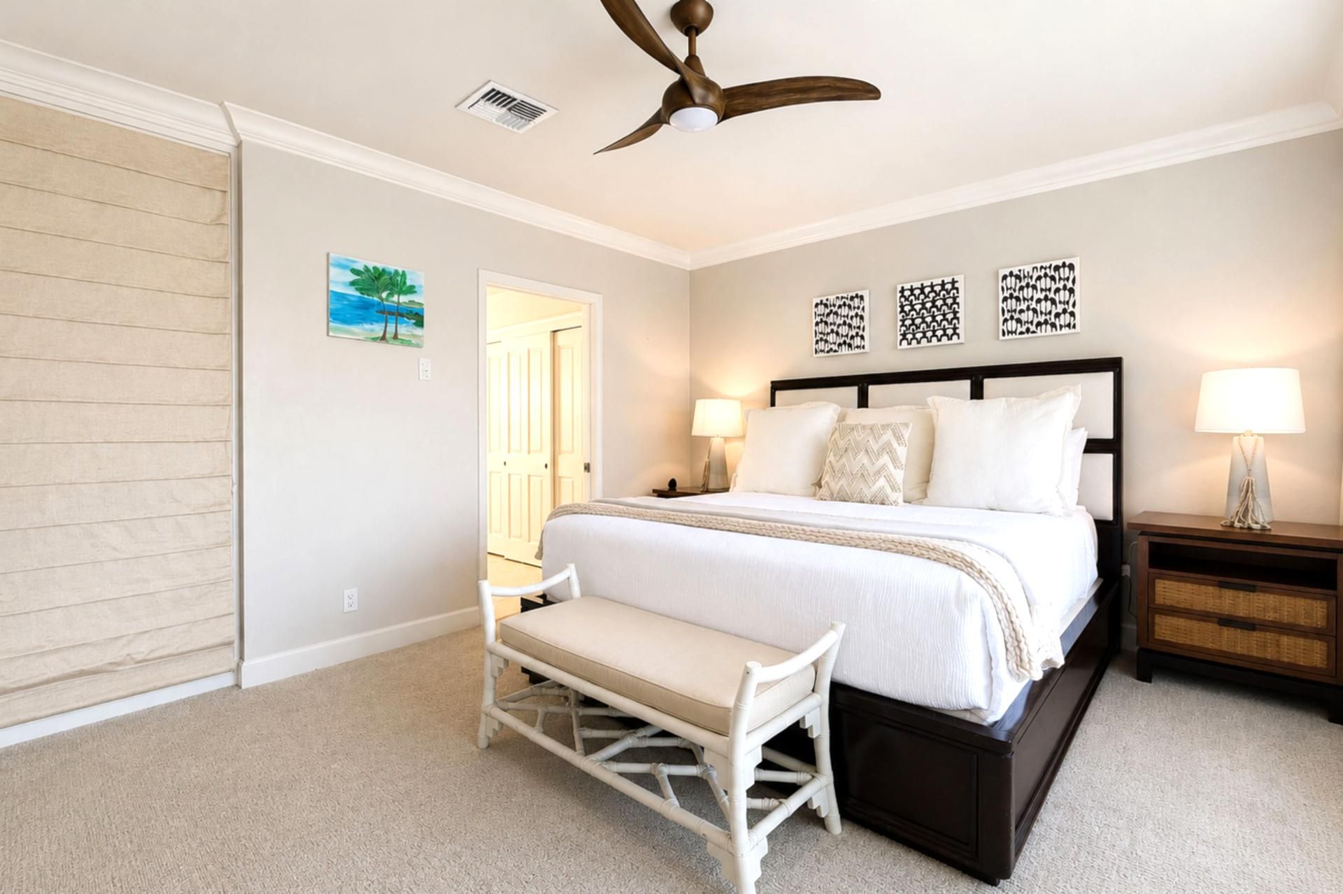 A bedroom with a bed, bedside tables, a bench, a ceiling fan, and artwork on the wall.