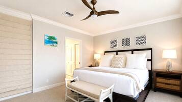 A bedroom with a bed, bedside tables, a bench, a ceiling fan, and artwork on the wall.