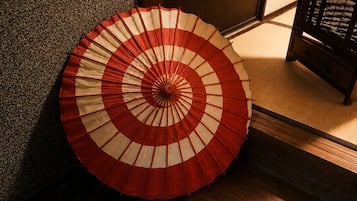 Ett traditionellt japanskt rum med tatamimattor på golvet, en trädörr och en röd- och vitrandig fläkt.
