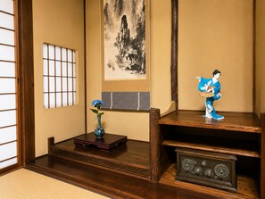 A traditional Japanese room with tatami flooring, a shoji screen, a calligraphy scroll, a vase with flowers, and a decorative figure.