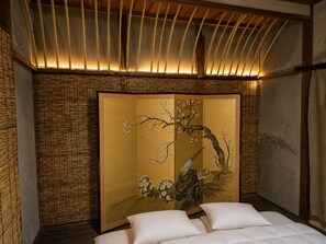 A traditional room with a tatami mat floor, a shoji screen with cherry blossoms, and a bed with white bedding.