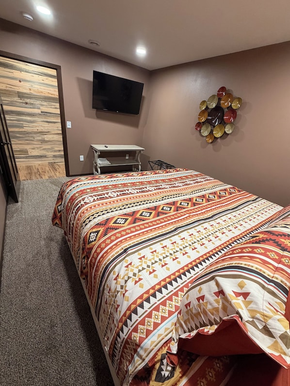 A bedroom with a bed, a television on the wall, a small table, and a decorative wall piece.
