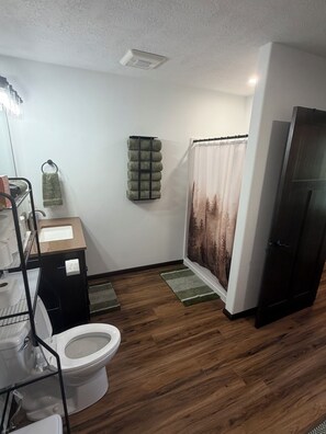 A bathroom with a toilet, a sink, a towel rack, a shower curtain, and a wooden floor.