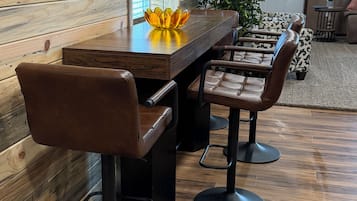 A dining area with a wooden table and bar stools, a potted plant, and a clock on the wall.