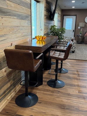 A dining area with a wooden table and bar stools, a potted plant, and a clock on the wall.