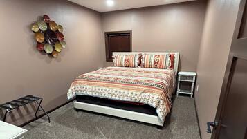 A bedroom with a bed, a small table, a chair, a wall decoration, and a door.
