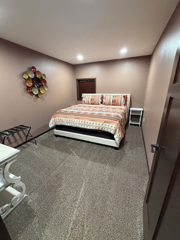 A bedroom with a bed, a small table, a chair, a wall decoration, and a door.