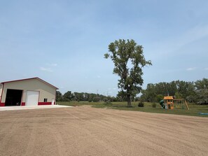 A large open area with a red and white building, a tall tree, and a playground structure. - The Back 40 Hideaway Huron, SD 5BR Getaway (Huron)