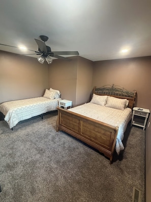 A bedroom with two single beds, a wooden headboard, a ceiling fan, and a small bedside table with a lamp.