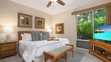 A bedroom with a bed, bedside tables, a television, and a window with a view of greenery.