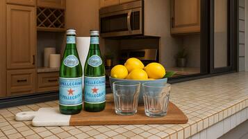 A kitchen counter with two Pellegrino water bottles, a bowl of lemons, and three glasses.