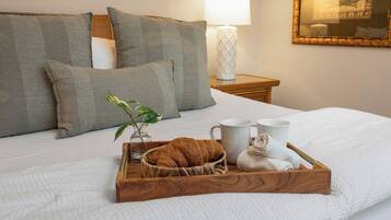 A neatly made bed with a tray of croissants, two white mugs, and a small plant.
