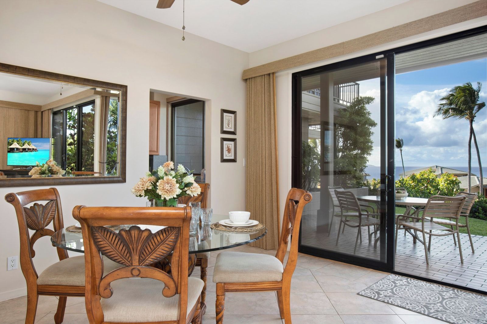 A dining area with a glass table, wooden chairs, and a view of the outdoors.