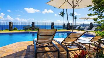 Uma área à beira da piscina com espreguiçadeiras, guarda-sóis e vista para o mar.