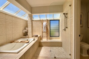 Een moderne badkamer met een badkuip, douche en toilet. Dakramen zorgen voor daglicht.