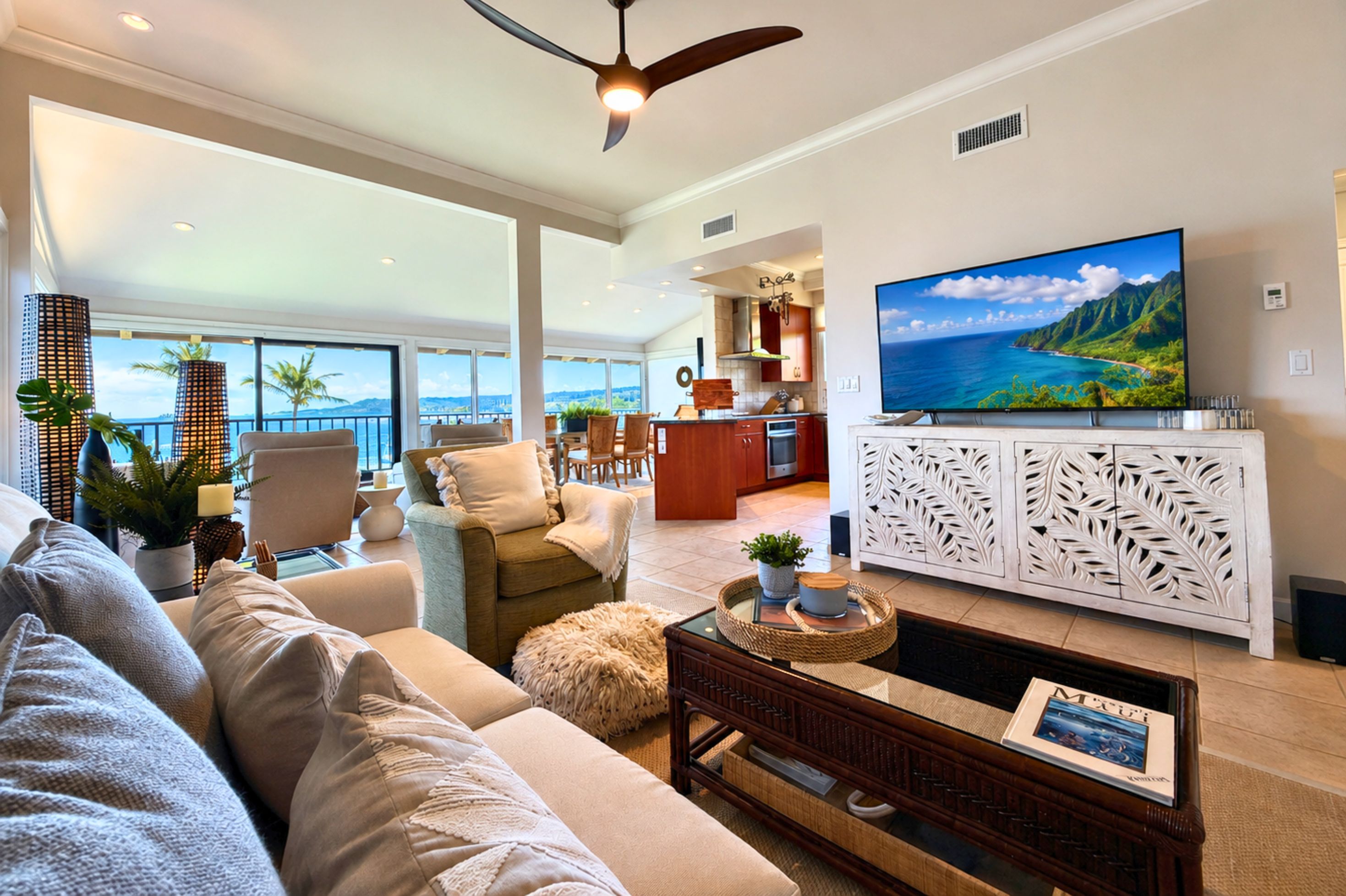 A spacious living area with a large sofa, a coffee table, and a television mounted on a white cabinet with intricate leaf patterns.