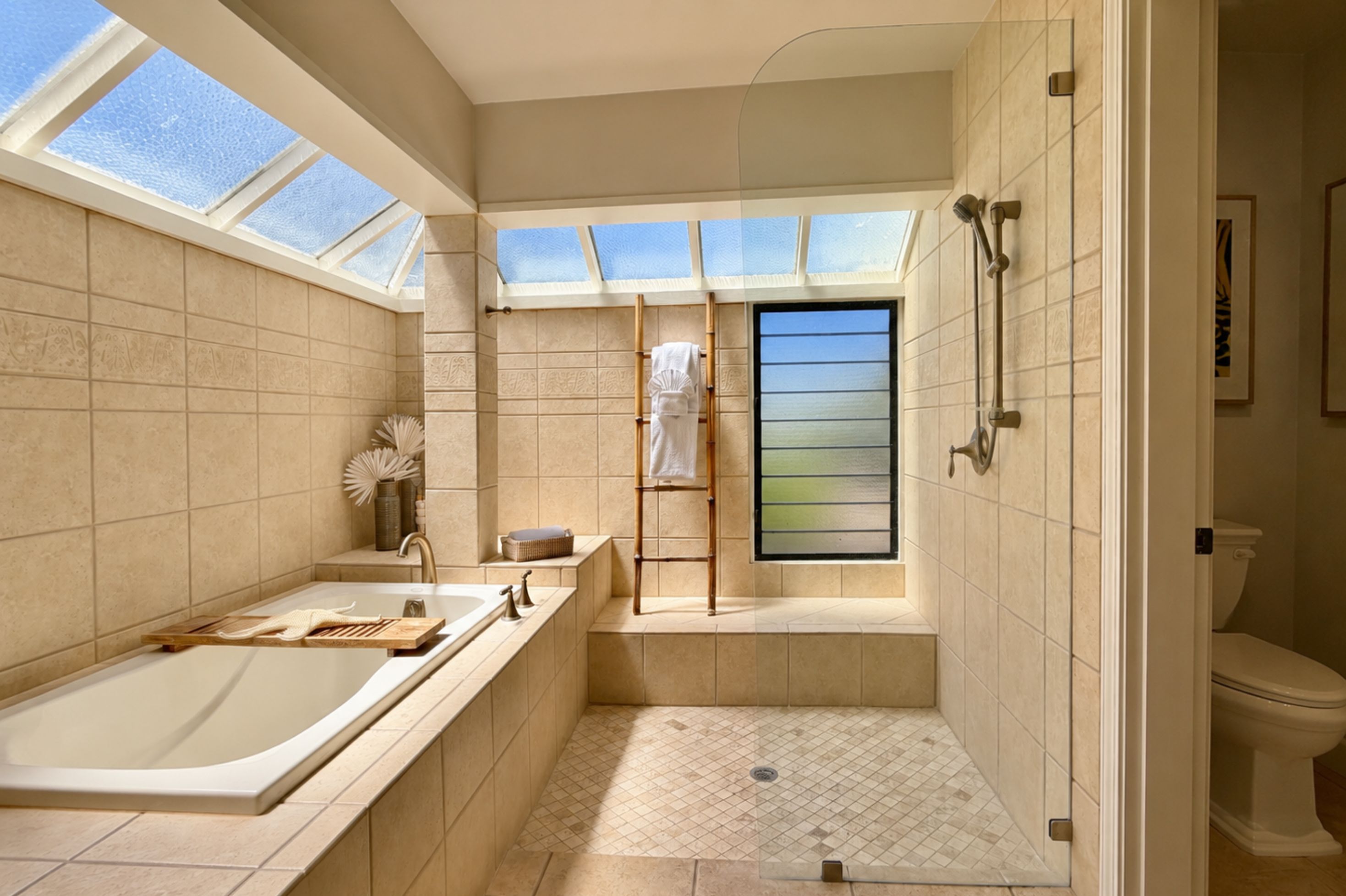 Une salle de bain moderne équipée d’une baignoire, d’une douche et de toilettes. Des fenêtres de toit permettent à la lumière naturelle d’entrer.