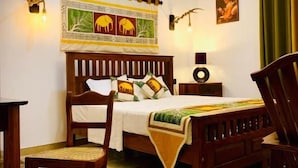 A bedroom with a wooden bed, a chair, a bedside table, and a wall tapestry. - Asoria Luxe Villa & Retreat (Kegalle)