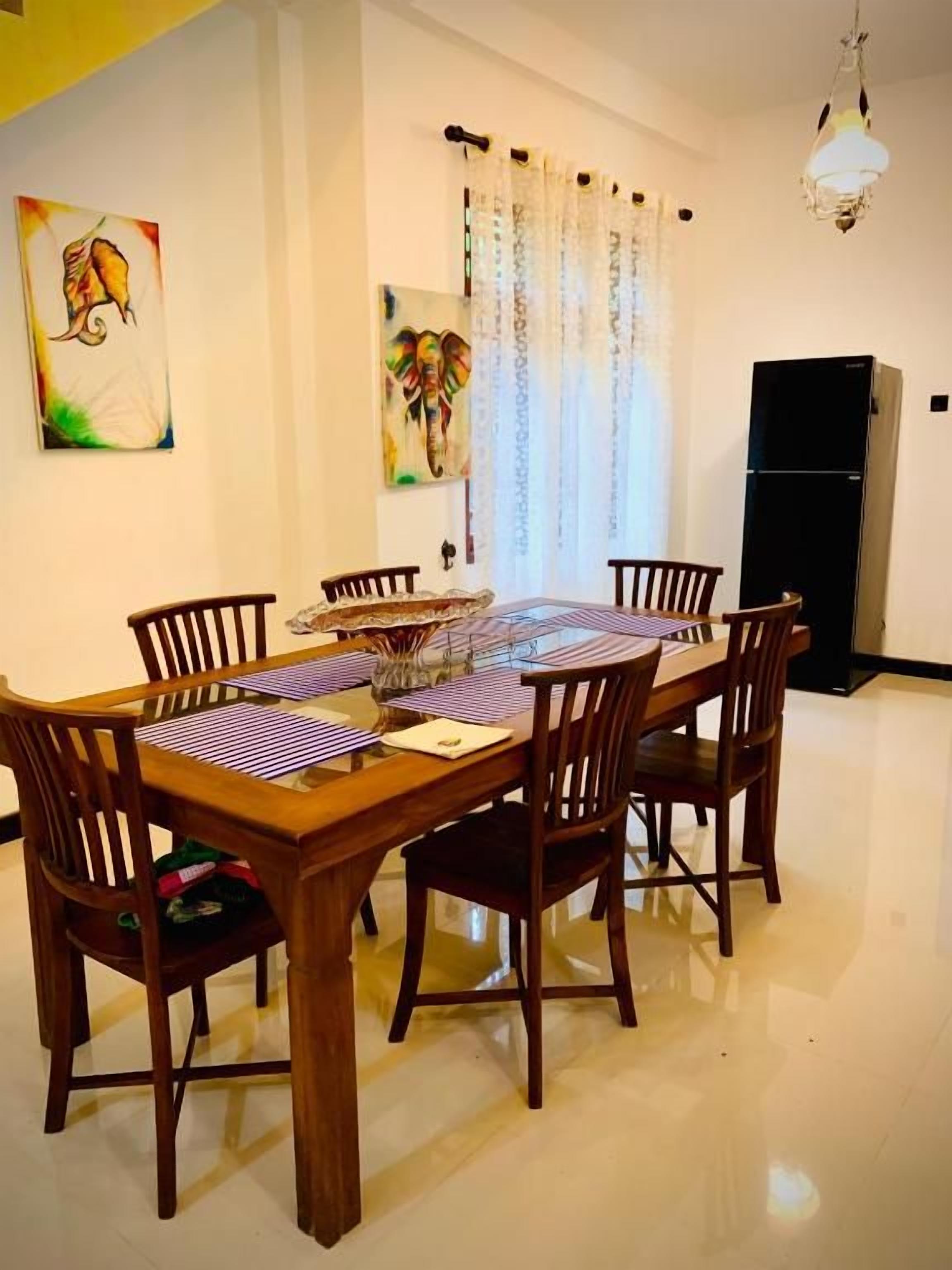 A dining area with a wooden table and chairs, a refrigerator, and artwork on the walls.