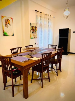 A dining area with a wooden table and chairs, a refrigerator, and artwork on the walls.