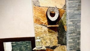 A bathroom with a stone wall, a mirror, a sink, and a toilet. - Asoria Luxe Villa & Retreat (Kegalle)