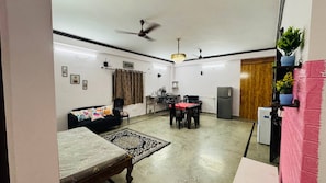 Una sala de estar con sofá, mesa de comedor y sillas, ventilador de techo y refrigerador.