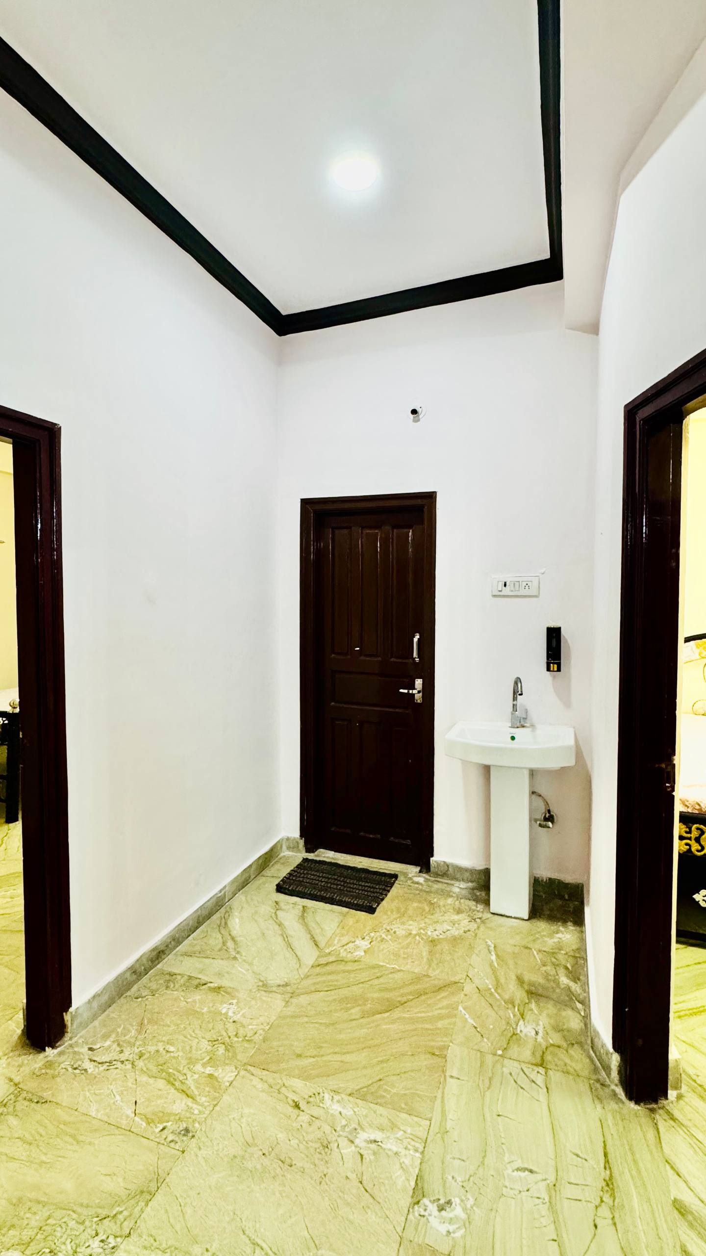 A hallway with a marble floor, a dark wooden door, and a white sink with a mirror.