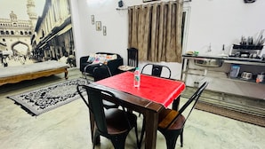 Uma sala de jantar com mesa vermelha, cadeiras pretas, tapete estampado e um mural na parede.