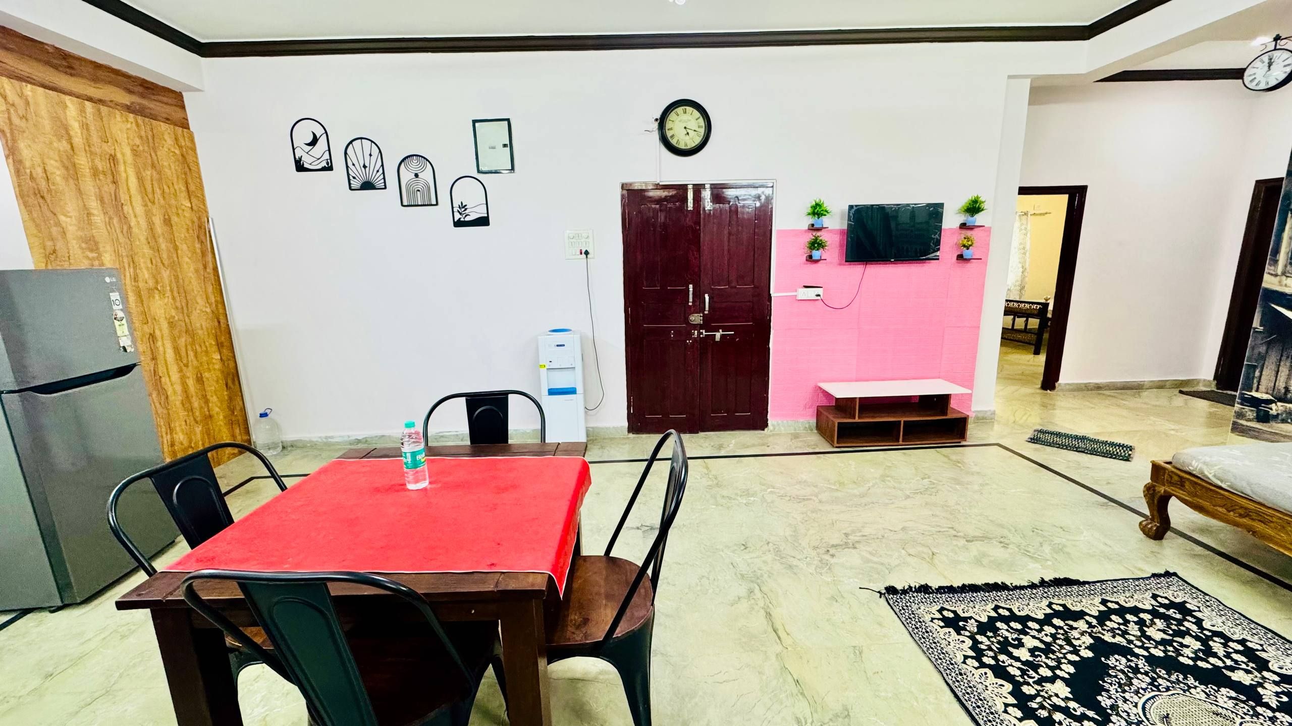 Una sala de estar con una mesa de comedor, sillas, refrigerador, dispensador de agua, reloj y una puerta.