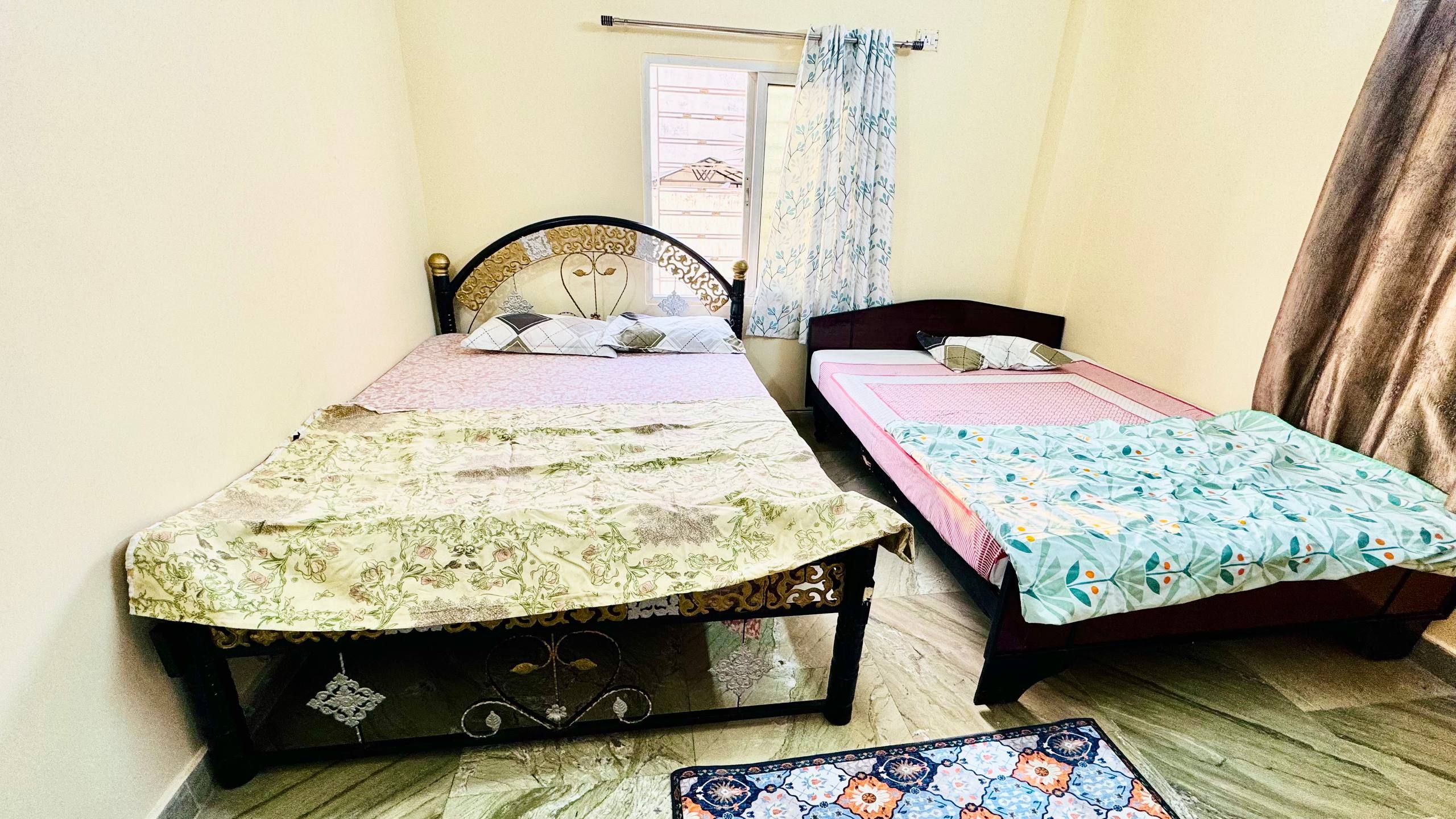 A small room with two single beds, a window with curtains, and a wooden floor.