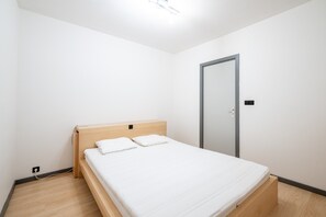 Ein kleines, sauberes Zimmer mit einem Einzelbett, einem Holz-Kopfteil und einer Tür.