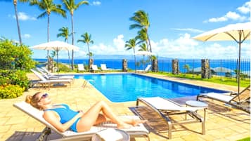 A poolside area with lounge chairs, umbrellas, and a view of the ocean.